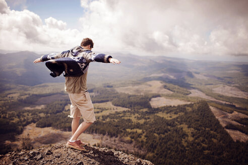 Man with arms outstretched standing on mountain against cloudy sky - CAVF34965