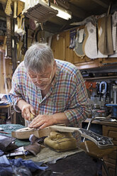 Craftsman shaping guitar at workbench in workshop - CAVF35045