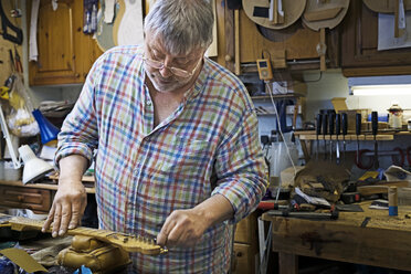 Craftsman working on strings of guitar at workshop - CAVF35048