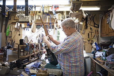 Handwerker misst das Griffbrett einer Gitarre an einer Werkbank in einer Werkstatt - CAVF35049