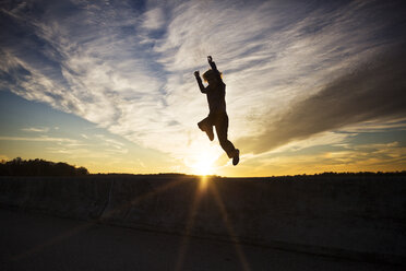 Silhouette eines Jungen, der bei Sonnenuntergang gegen den Himmel springt - CAVF35093