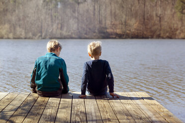 Rear view of boys sitting on pier over lake - CAVF35115