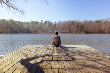 Rückansicht eines jugendlichen Mädchens, das am Rande eines Stegs über dem See sitzt - CAVF35118
