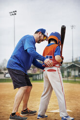 Seitenansicht eines Trainers, der einem Jungen beim Baseballspielen auf dem Feld hilft - CAVF35123