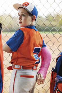 Side view of baseball player with fractured hand standing by chainklink fence on field - CAVF35125