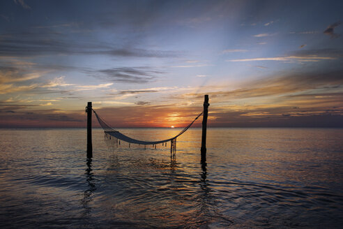 Hammock tied to wooden poles on sea during sunset - CAVF35137