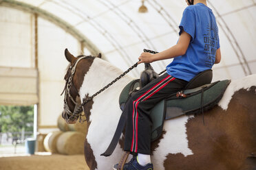 Seitenansicht tiefer Ausschnitt eines Jungen, der auf einem Pferd in einer Ranch sitzt - CAVF35142