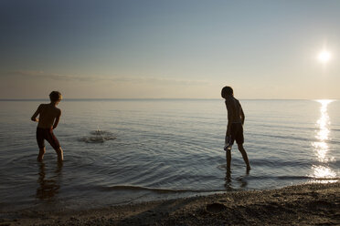 Rückansicht von Jungen, die bei Sonnenuntergang am Strand spielen - CAVF35153