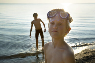 Porträt eines Jungen mit Schwimmbrille am Ufer mit einem Freund im Hintergrund - CAVF35154