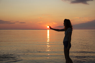 Silhouette eines Teenagers, der am Strand steht und die Sonne berührt - CAVF35158