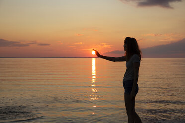 Silhouette of teenage girl touching sun while standing on beach - CAVF35158