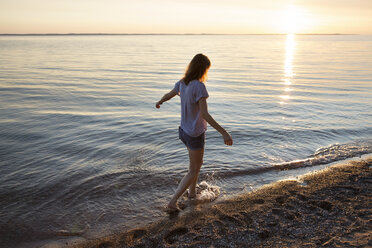 Full length of teenage girl walking on shore at beach during sunset - CAVF35159