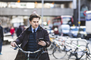 UK, London, Geschäftsmann schiebt Fahrrad in der Stadt und schaut auf sein Handy - WPEF00162