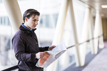 Businessman standing in skywalk reading newspaper - WPEF00168