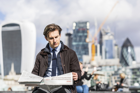UK, London, Porträt eines seriösen Geschäftsmannes beim Lesen einer Zeitung, lizenzfreies Stockfoto