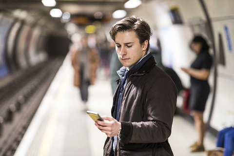 UK, London, Geschäftsmann wartet in der U-Bahn-Station und benutzt ein Handy, lizenzfreies Stockfoto