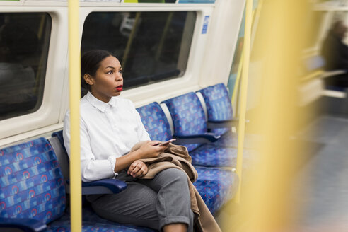 UK, London, Geschäftsfrau mit Mobiltelefon in der U-Bahn sitzend - MAUF01366