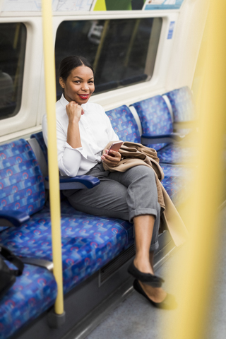 UK, London, portrait of smiling businesswoman with cell phone sitting in underground train stock photo