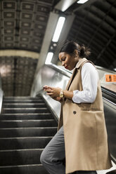 UK, London, lächelnde Geschäftsfrau steht auf der Rolltreppe einer U-Bahn-Station und schaut auf ihr Mobiltelefon - MAUF01370