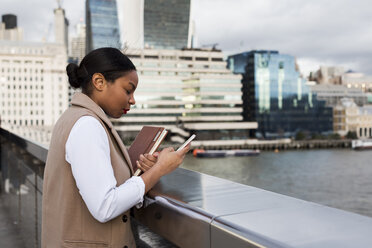 UK, London, businesswoman standing on bridge using cell phone - MAUF01379