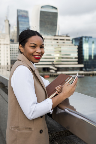 UK, London, portrait of smiling businesswoman standing on bridge with cell phone stock photo