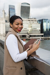 UK, London, portrait of smiling businesswoman standing on bridge with cell phone - MAUF01380