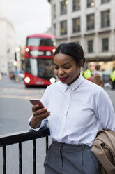 Großbritannien, London, lächelnde Geschäftsfrau mit Blick auf ihr Handy - MAUF01382