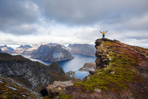 Norwegen, Lofoten, Reine, Mann mit erhobenen Armen auf Reinebringen, lizenzfreies Stockfoto