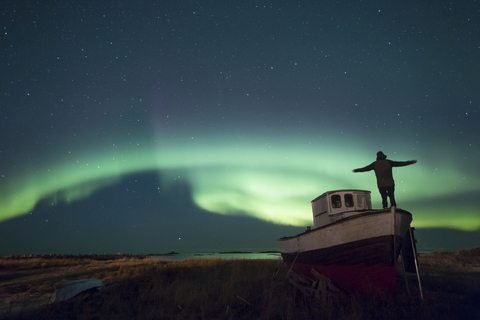 Norway, Lofoten Islands, Eggum, man admiring northern lights, standing on fishing boat stock photo