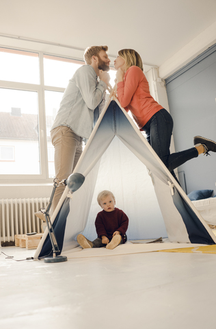 Happy couple kissing over tent with their son sitting in it stock photo