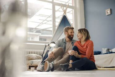 Affectionate couple sitting on ground, smiling happily - KNSF03745