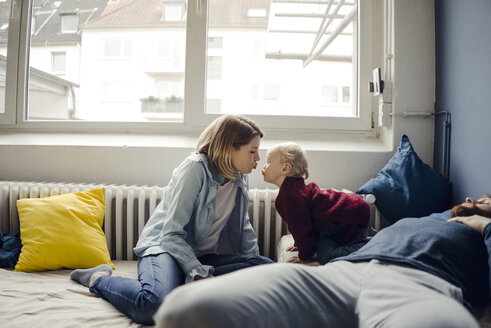 Familie entspannt sich zu Hause auf dem Sofa, Mutter küsst ihren kleinen Sohn - KNSF03757