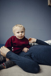 Vater und Sohn ruhen sich auf der Couch aus, das Baby sitzt auf dem Gesicht des Vaters - KNSF03758