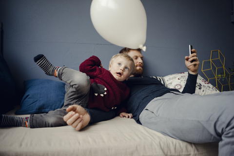 Vater liest SMS, während sein Sohn mit einem Luftballon spielt, lizenzfreies Stockfoto