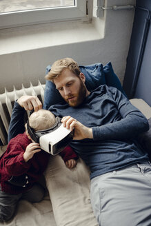 Father and son playing with VR glasses at home - KNSF03761