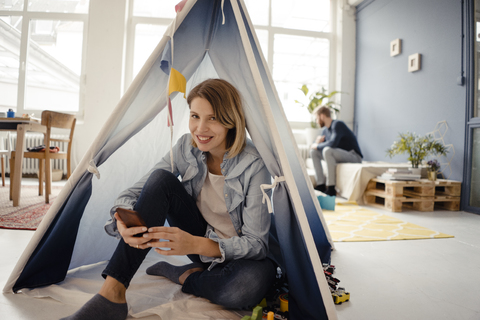 Woman using smartphone in a toy tent, husband sitting in background stock photo