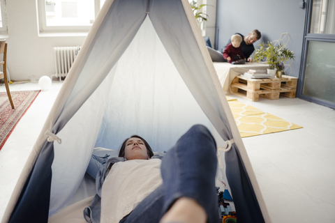 Frau ruht sich im Zelt aus, während der Vater im Hintergrund mit seinem Sohn spielt, lizenzfreies Stockfoto