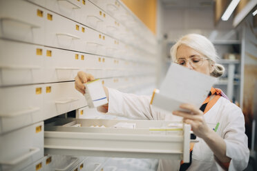 Ältere Apothekerin hält Rezeptpapier und prüft Medikamente in einer Schublade im Laden - MASF00388