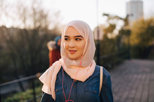 Selbstbewusste junge muslimische Frau hört Musik und schaut in die Ferne gegen den klaren Himmel - MASF00395