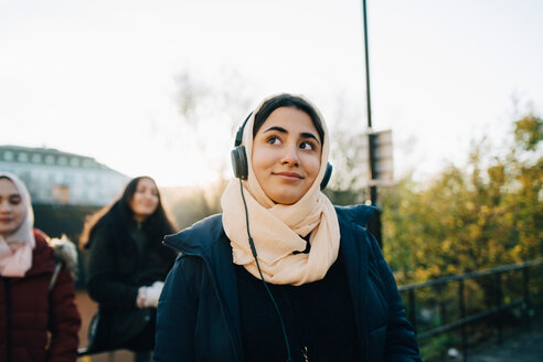 Lächelndes Teenager-Mädchen, das mit Freunden Kopfhörer hört, gegen den Himmel - MASF00398