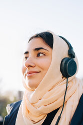 Low angle view of smiling teenage girl listening music through headphones against clear sky - MASF00400
