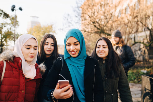 Glückliche junge Frau teilt ihr Smartphone mit multiethnischen Freunden in der Stadt - MASF00406