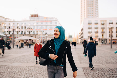 Lächelnde junge muslimische Frau mit Hidschab auf dem Fußweg in der Stadt - MASF00411