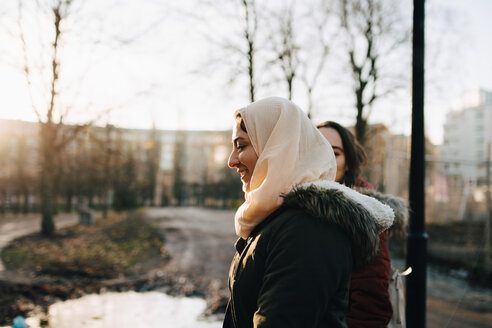 Seitenansicht einer lächelnden jungen muslimischen Frau mit einer Freundin beim Spaziergang in der Stadt bei Sonnenuntergang - MASF00415