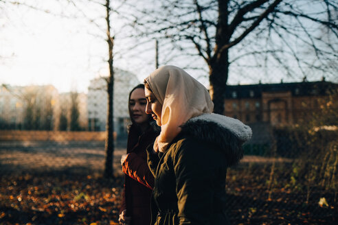 Seitenansicht von jungen muslimischen Freundinnen, die bei Sonnenuntergang in der Stadt spazieren gehen - MASF00416