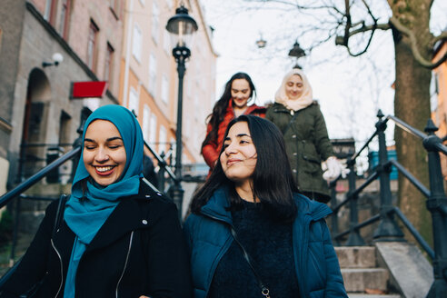 Niedriger Blickwinkel auf lächelnde multiethnische Freundinnen, die sich auf einer Treppe in der Stadt nach unten bewegen - MASF00417