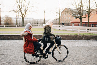 Seitenansicht einer jungen Frau, die mit einer Freundin auf der Straße Fahrrad fährt - MASF00428