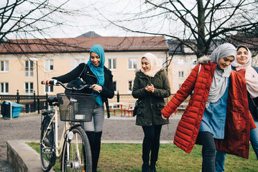 Glückliche multiethnische Freundinnen gehen mit dem Fahrrad auf einer Wiese in der Stadt spazieren - MASF00430