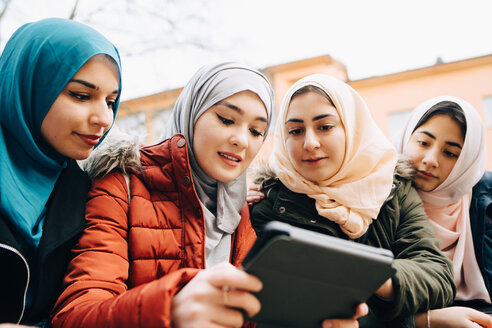 Niedriger Blickwinkel auf multiethnische muslimische Freunde, die sich ein digitales Tablet teilen - MASF00434