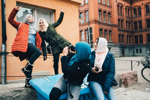 Junge Frau fotografiert fröhliche Freundinnen vor einem Gebäude in der Stadt - MASF00439